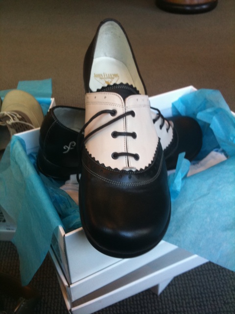 Black and cream saddle shoes sit on an open Fluevog shoebox.